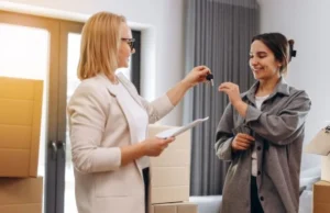 Two women exchanging keys in a room with boxes