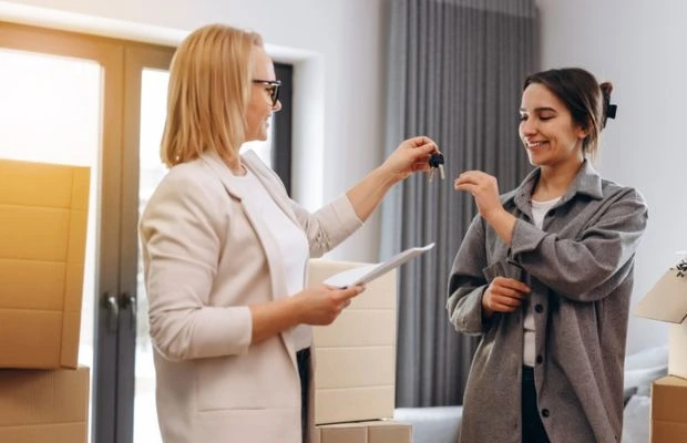 Two women exchanging keys in a room with boxes